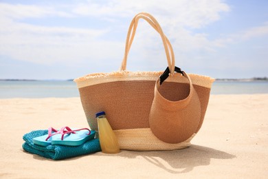 Beach accessories and bottle of refreshing drink on sand near sea