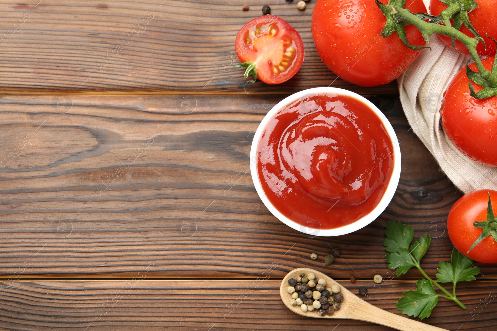 Photo of Delicious ketchup in bowl, tomatoes and peppercorns on wooden table, flat lay. Space for text