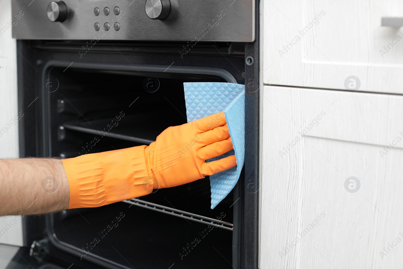 Photo of Young man cleaning oven with rag in kitchen, closeup