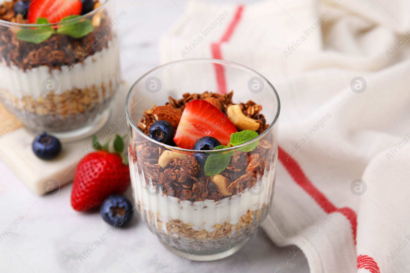 Photo of Tasty granola with berries, nuts, yogurt and chia seeds in glasses on white marble table, closeup