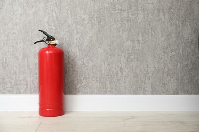 Photo of Fire extinguisher on floor near grey wall, space for text