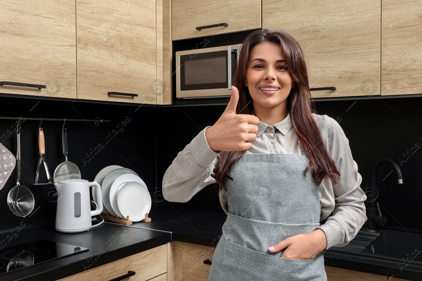 Photo of Young woman in green apron showing thumb up indoors, space for text