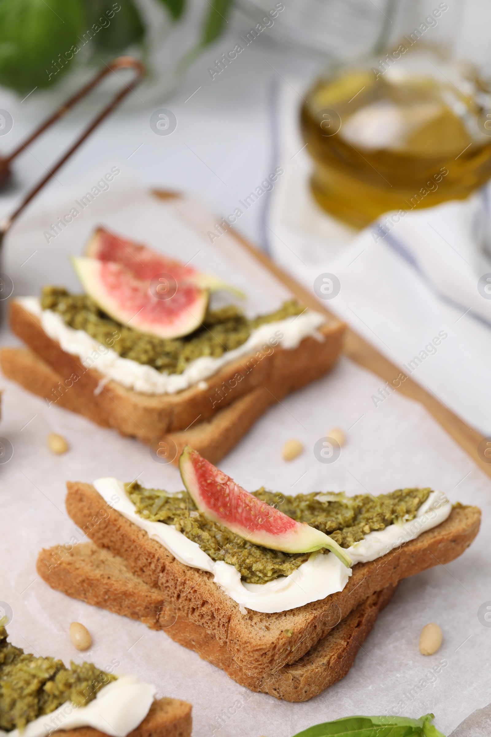 Photo of Tasty bruschetta with cream cheese, pesto sauce and fig on parchment paper