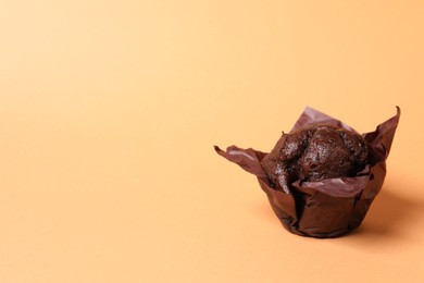 Photo of Tasty chocolate muffin on pale orange background, space for text