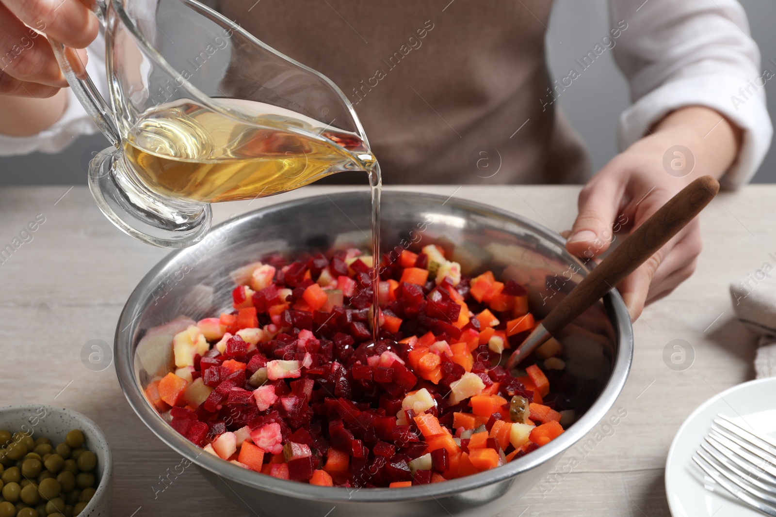 Photo of Woman dressing delicious vinaigrette salad at light wooden table, closeup