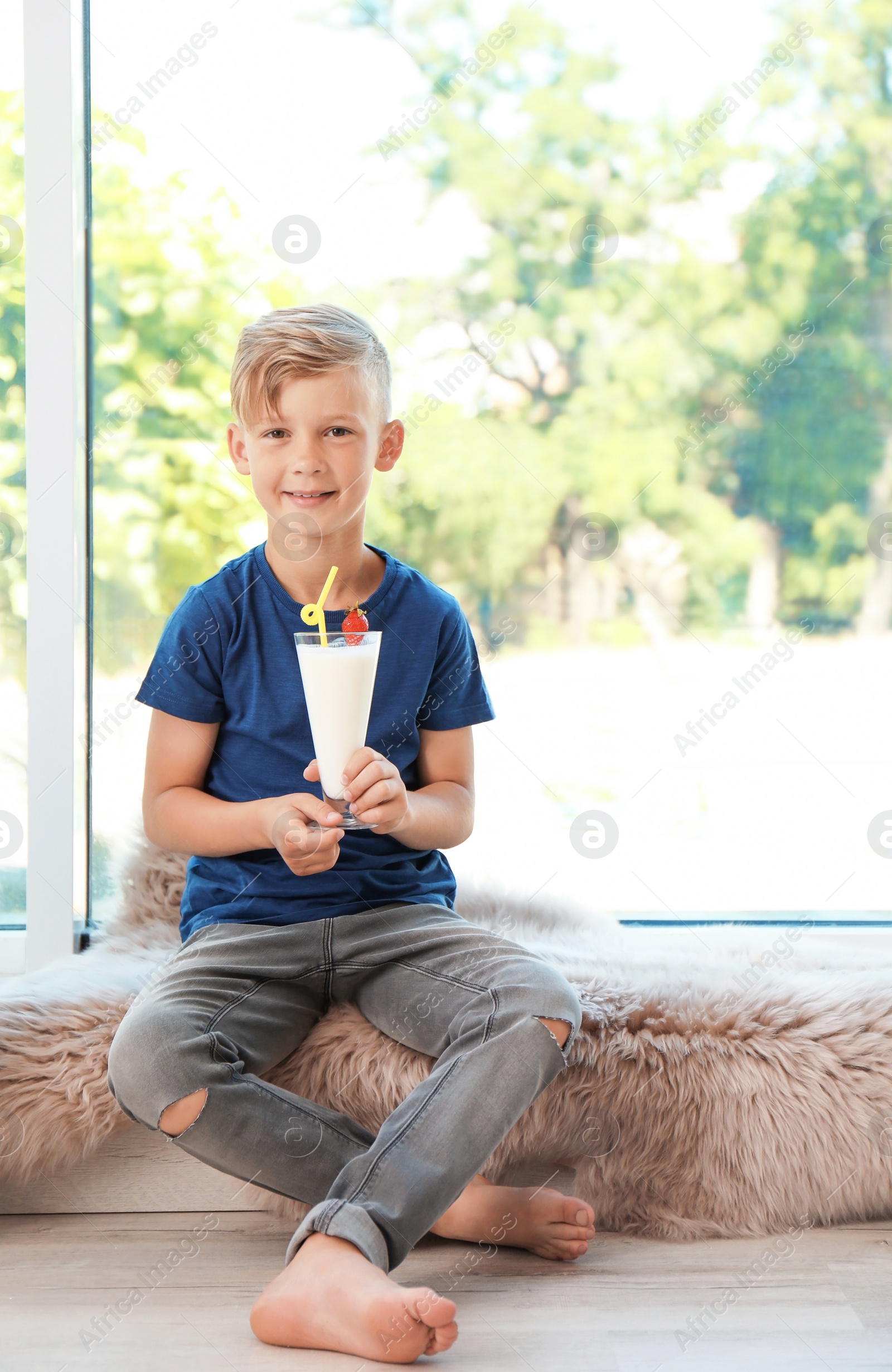 Photo of Little boy with glass of milk shake near window indoors