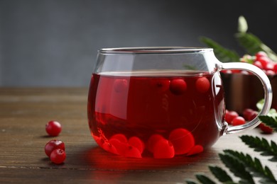 Photo of Tasty hot cranberry tea in glass and fresh berries on wooden table