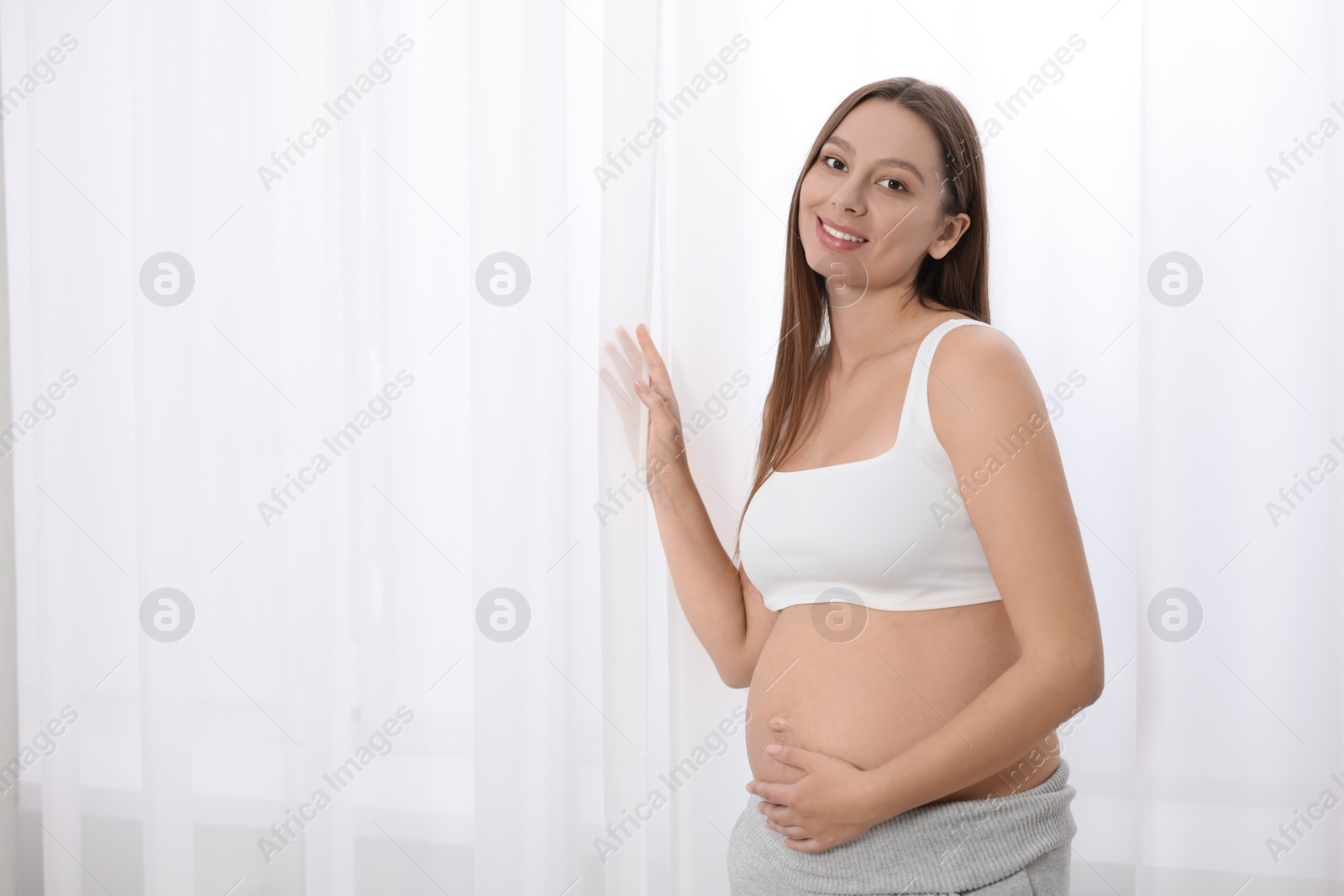 Photo of Beautiful pregnant woman near window indoors, space for text