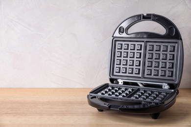 Photo of Modern waffle iron on wooden table against white background. Space for text