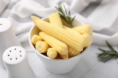 Photo of Tasty fresh yellow baby corns in bowl on white tiled table, closeup