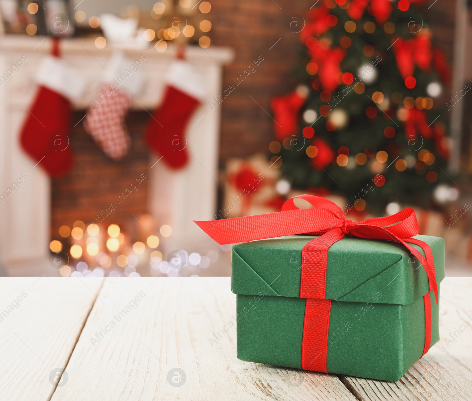 Image of Christmas gift box on white wooden table in room, bokeh effect. Space for text