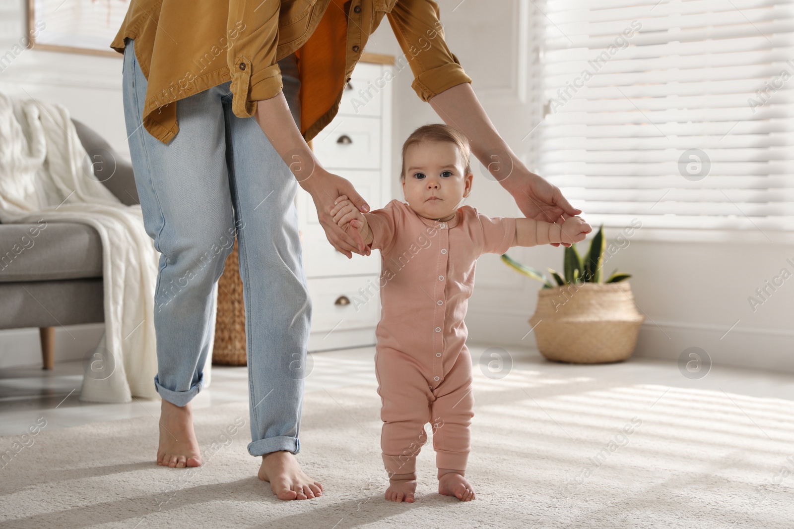 Photo of Mother supporting her baby daughter while she learning to walk at home