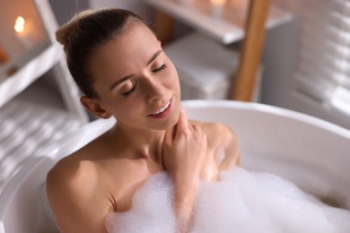 Photo of Beautiful woman taking bath in tub with foam indoors. Space for text