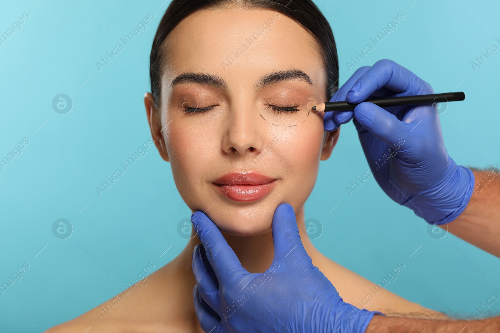 Photo of Doctor with pencil preparing patient for cosmetic surgery operation on light blue background, closeup