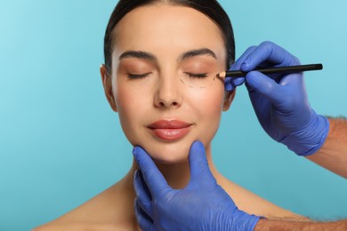 Doctor with pencil preparing patient for cosmetic surgery operation on light blue background, closeup