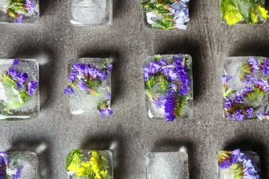 Ice cubes with flowers on grey stone background, flat lay