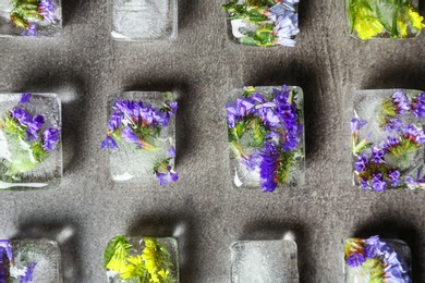 Photo of Ice cubes with flowers on grey stone background, flat lay