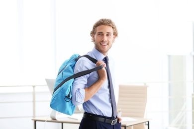 Photo of Young handsome businessman holding fitness bag in office. Gym after work