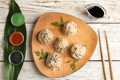 Flat lay composition with plate of tasty baozi dumplings and sauces on white wooden table