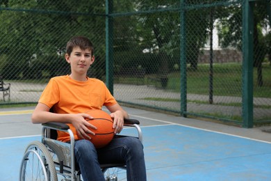 Photo of Disabled teenage boy in wheelchair with basketball ball at outdoor court