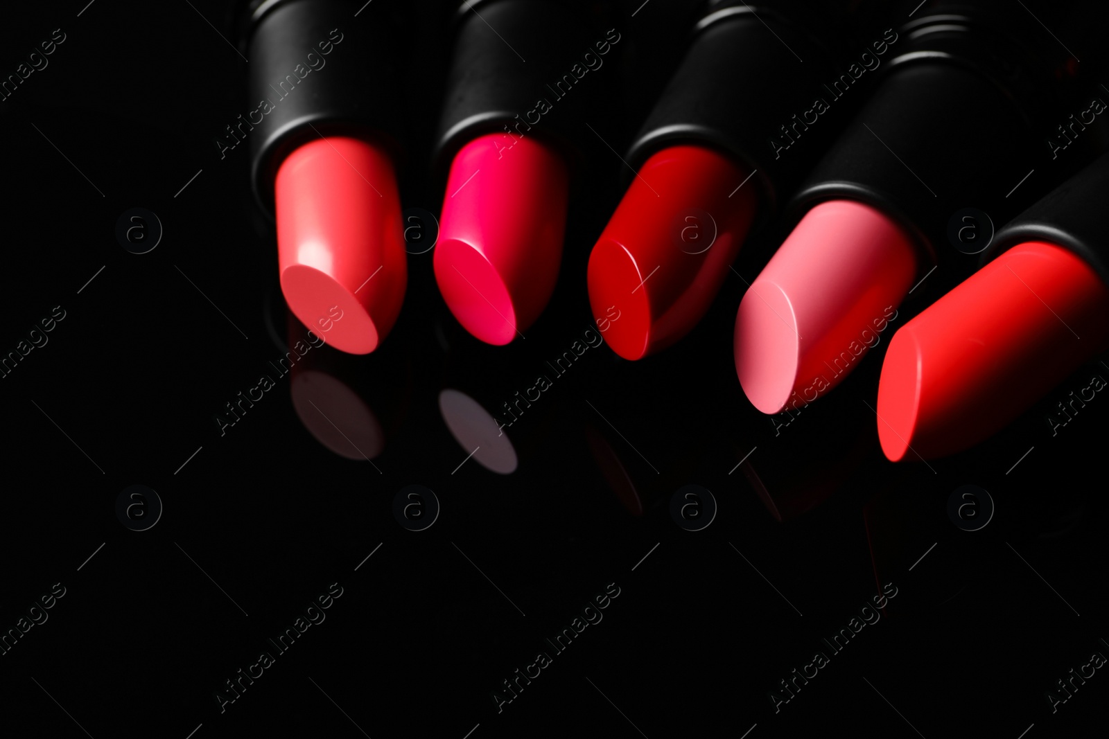 Photo of Many bright lipsticks on black glass surface, space for text