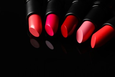 Photo of Many bright lipsticks on black glass surface, space for text