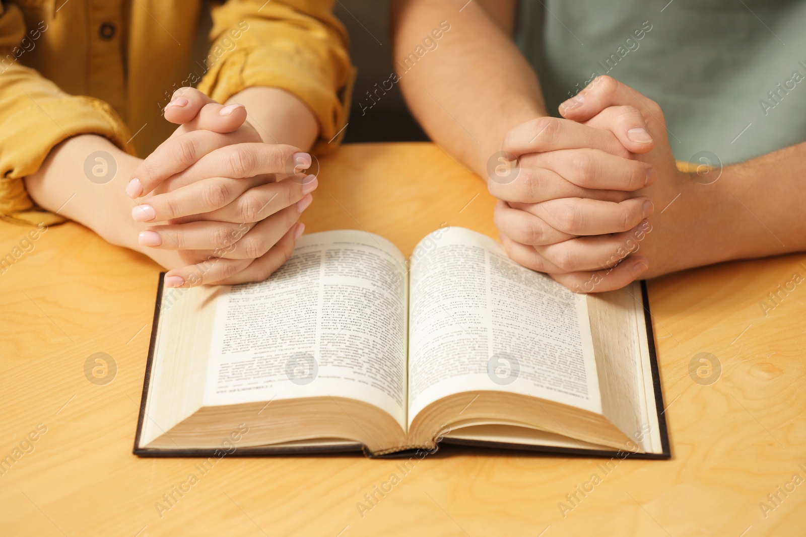 Photo of Family couple praying over Bible together at table indoors, closeup