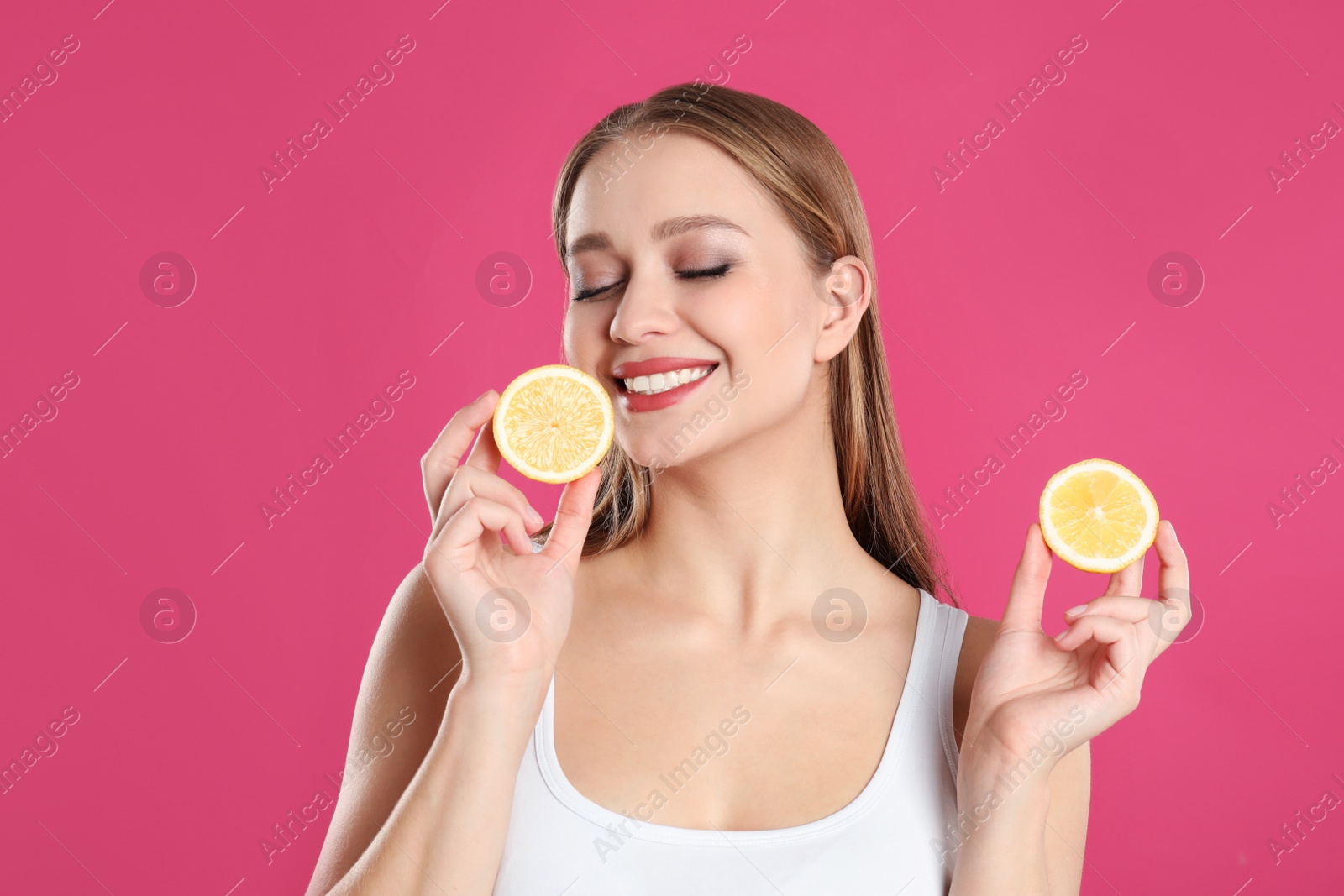 Photo of Young woman with cut lemon on pink background. Vitamin rich food