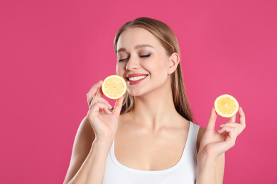 Photo of Young woman with cut lemon on pink background. Vitamin rich food