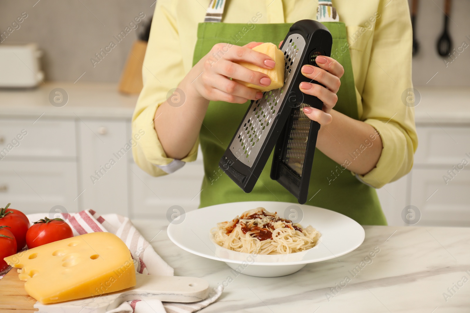 Photo of Woman grating cheese onto delicious pasta at white marble table in kitchen, closeup