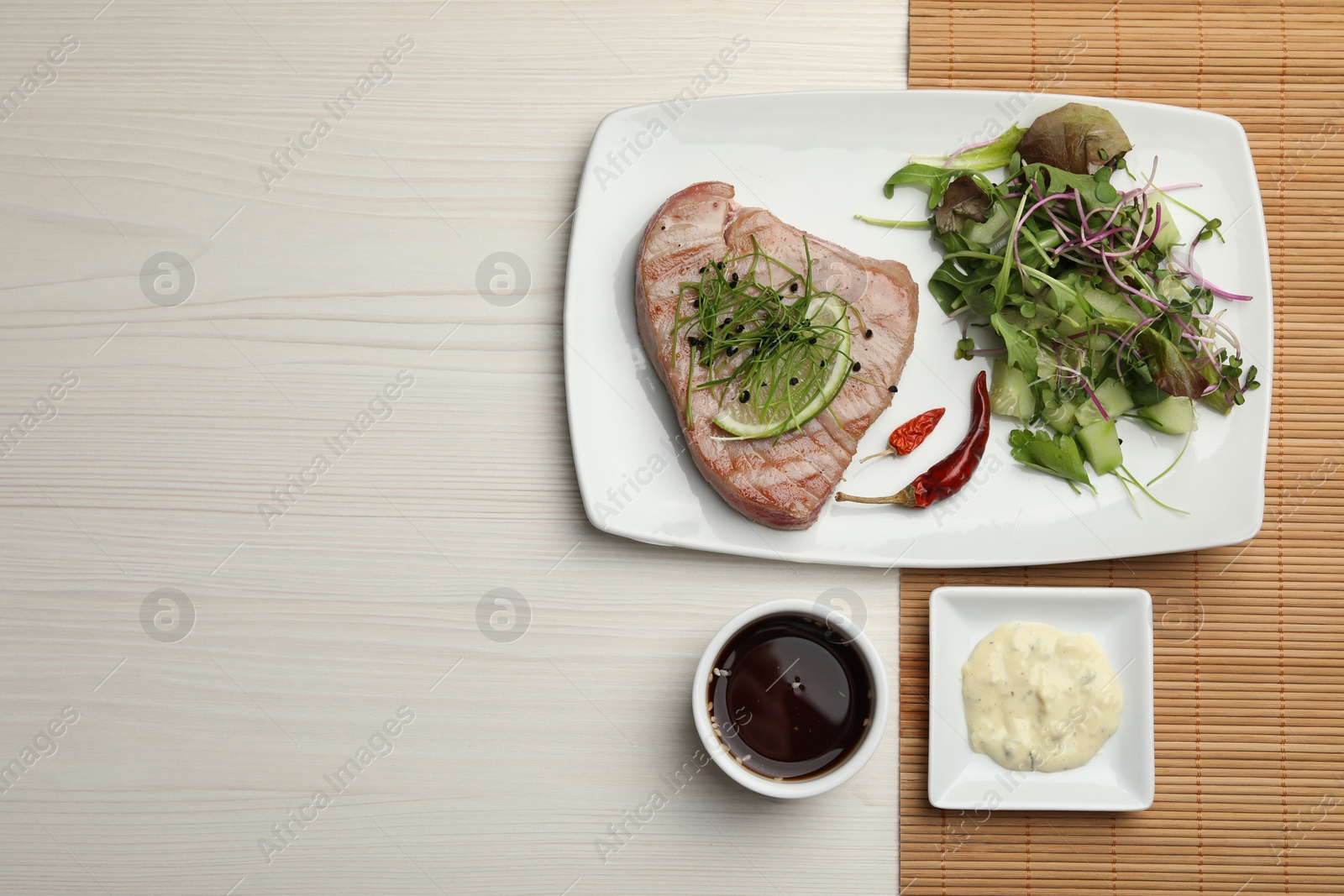 Photo of Delicious tuna steak served with salad and sauces on white wooden table, flat lay. Space for text