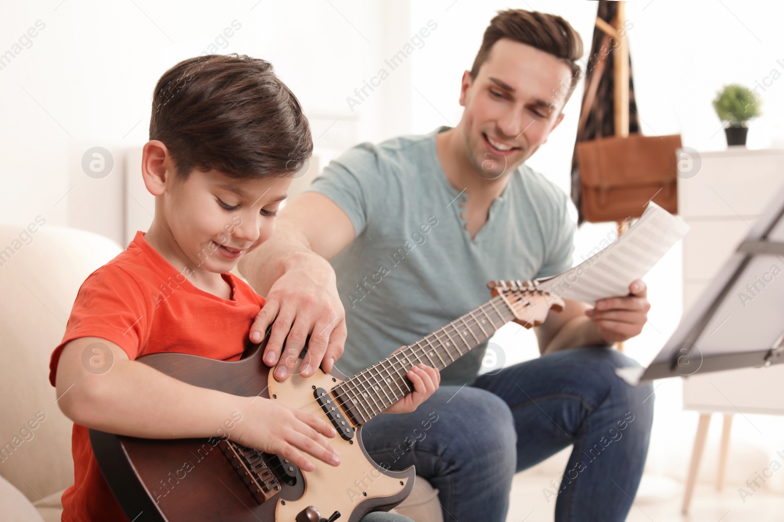 Photo of Little boy playing guitar with his teacher at music lesson. Learning notes