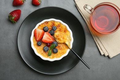 Delicious creme brulee with berries and mint in bowl served on grey table, flat lay
