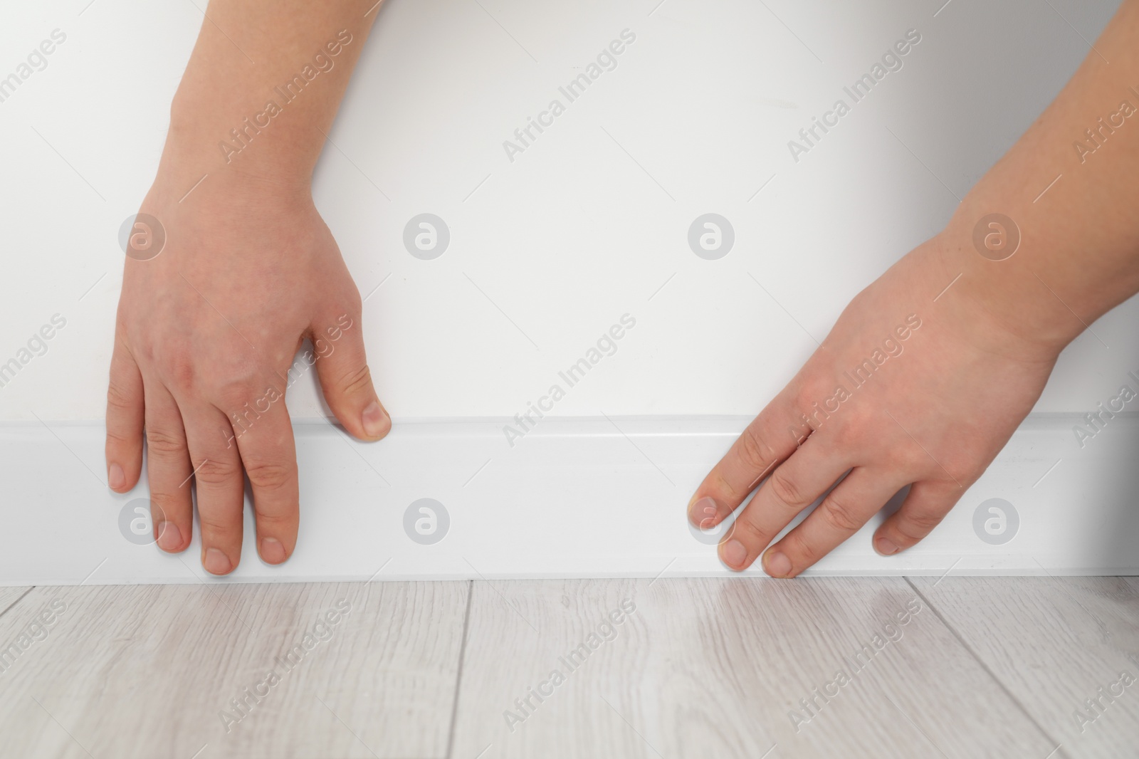 Photo of Man installing plinth on laminated floor in room, closeup