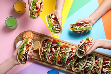 Photo of Friends holding delicious tacos on color background, top view