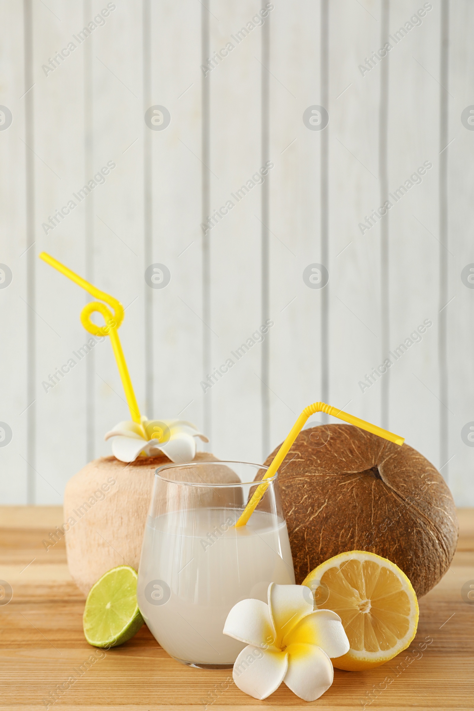 Photo of Composition with glass of coconut water on wooden table against light background