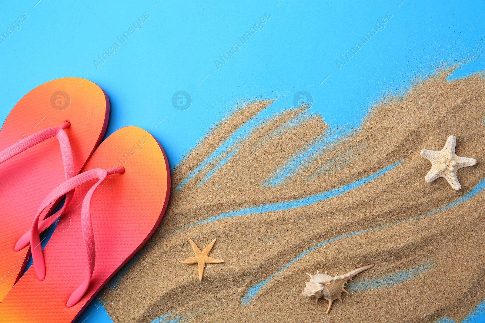 Photo of Flip flops and sand on light blue background, flat lay. Beach accessories