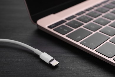Photo of USB cable with lightning connector and laptop on black wooden table, closeup