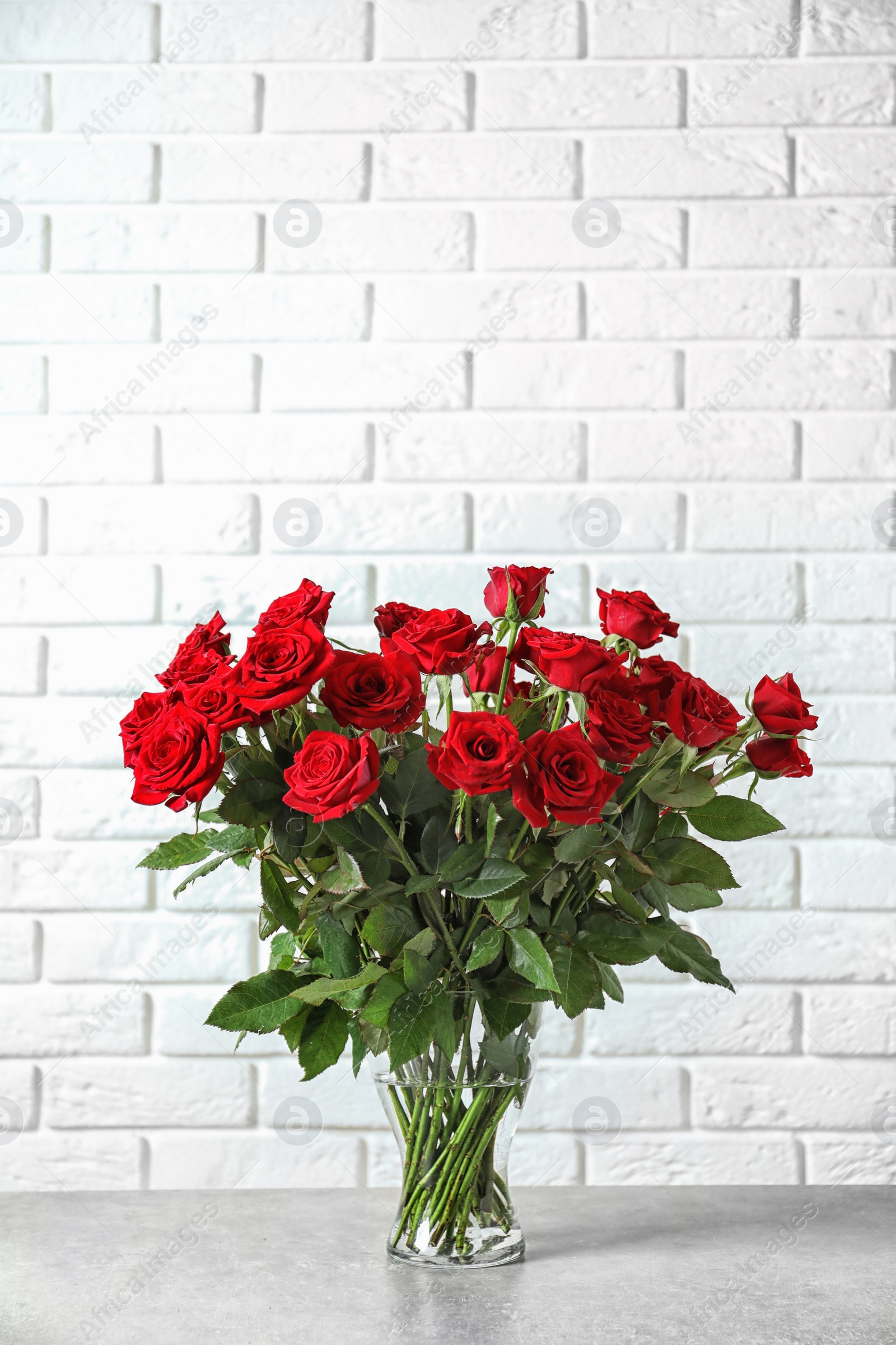 Photo of Vase with beautiful red roses on table against brick wall background