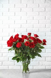 Photo of Vase with beautiful red roses on table against brick wall background