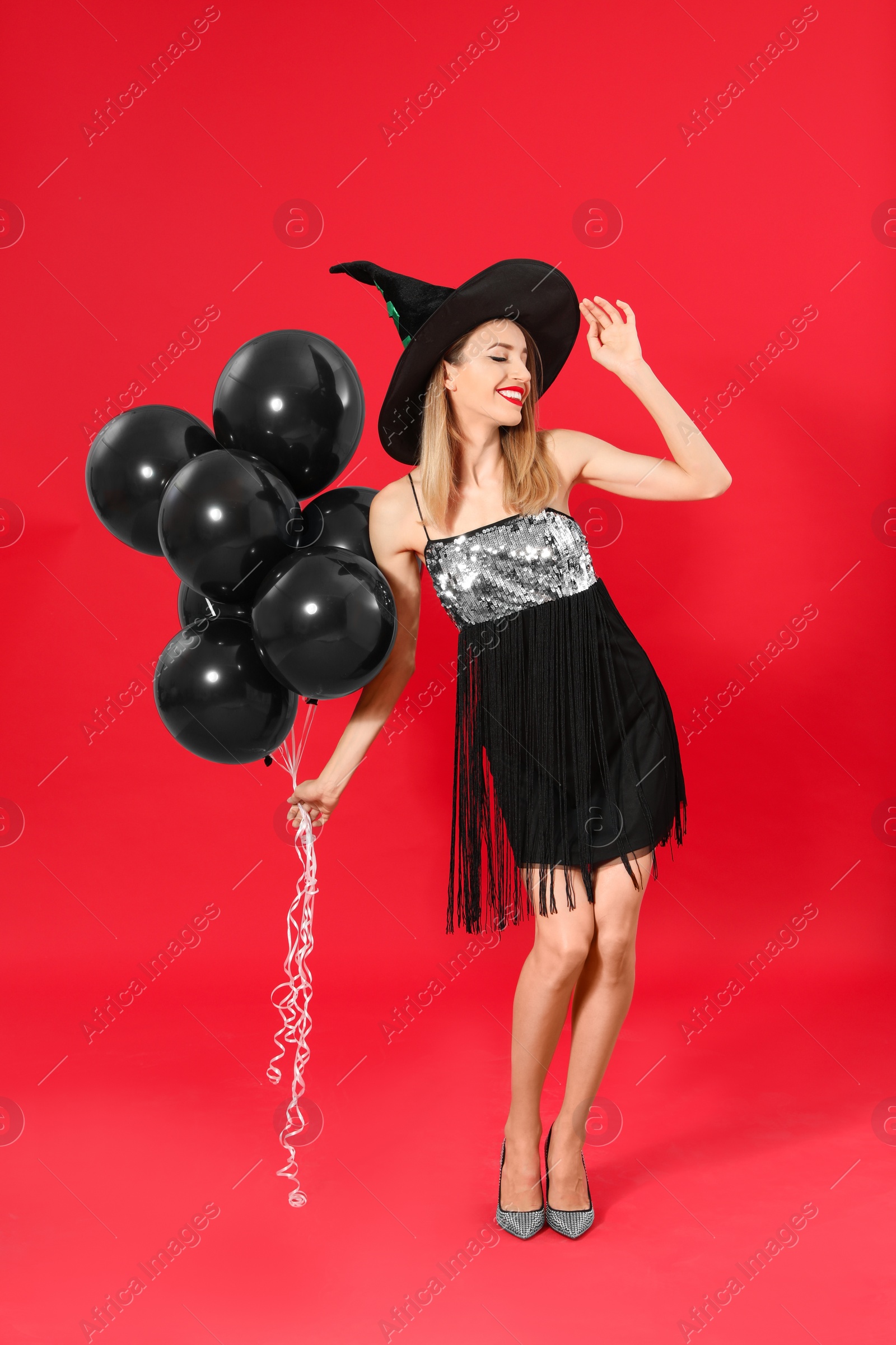 Photo of Beautiful woman wearing witch costume with balloons for Halloween party on red background