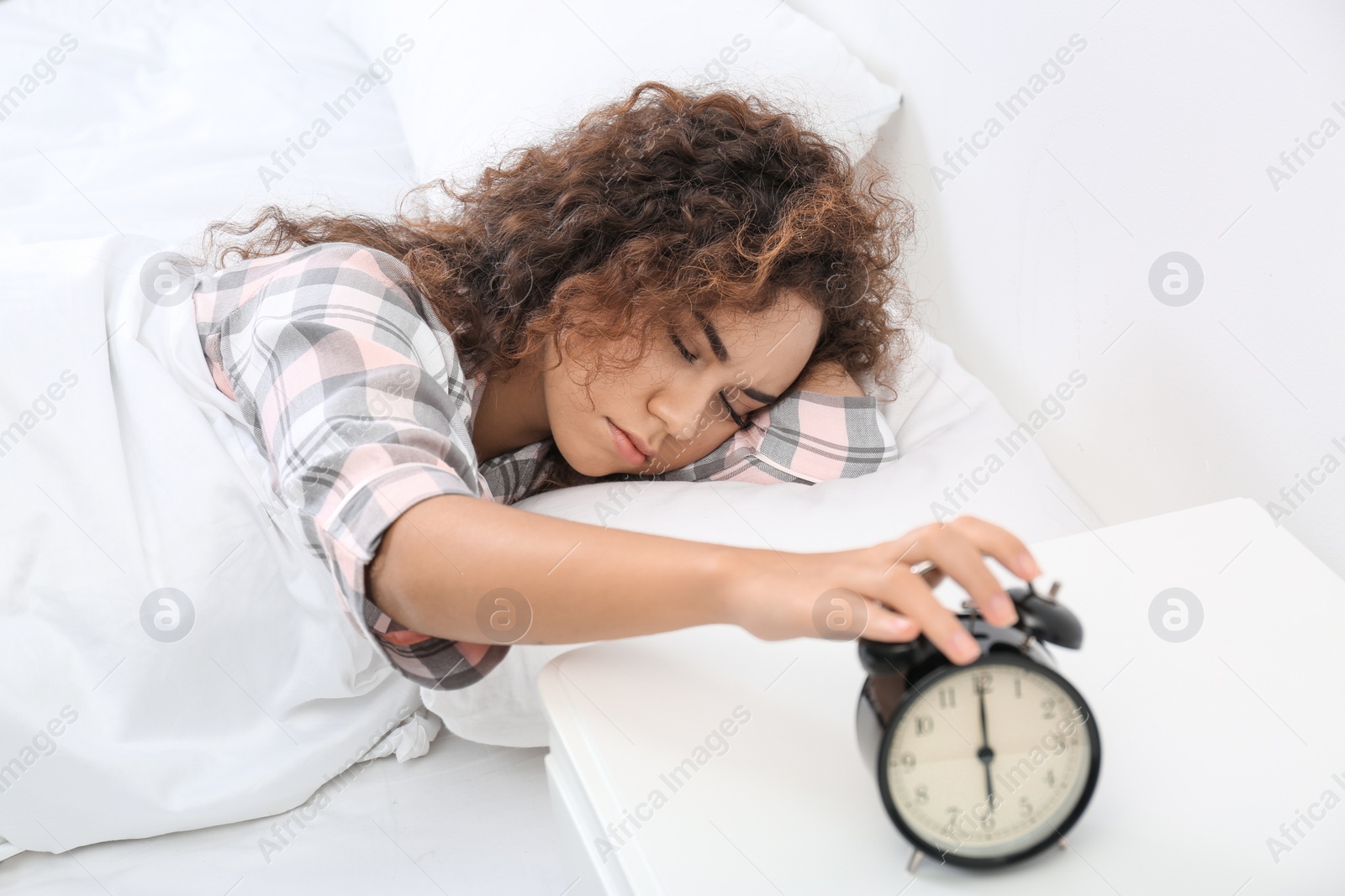 Photo of Young African-American woman turning off alarm clock at home. Bedtime