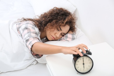 Young African-American woman turning off alarm clock at home. Bedtime