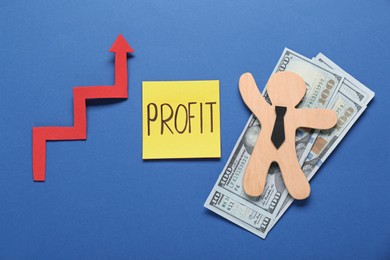Photo of Sticky note with word Profit, up arrow, wooden human figure and banknotes on blue background, flat lay