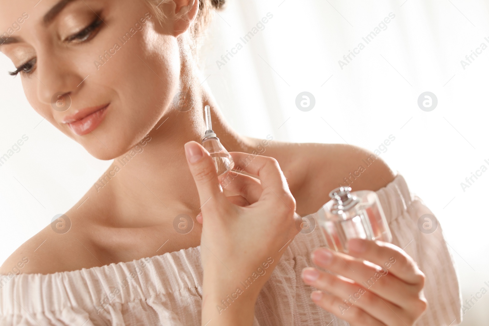 Photo of Young woman applying perfume on neck against blurred background