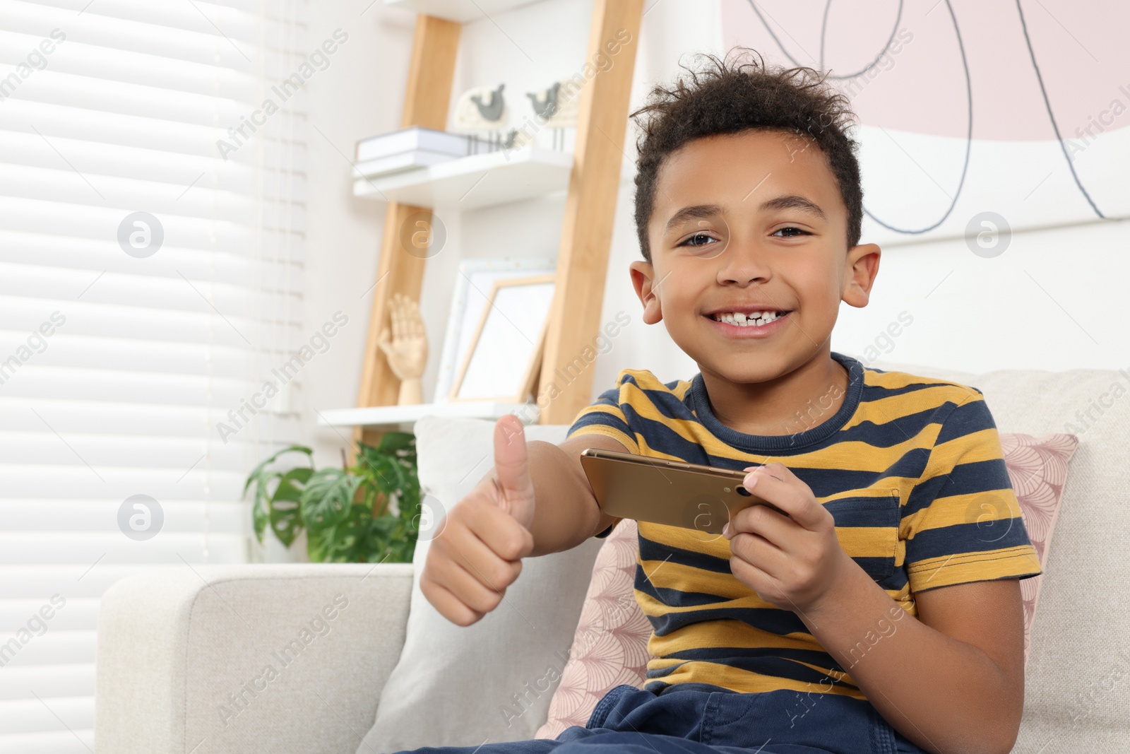 Photo of Cute African-American boy playing on phone at home. Space for text