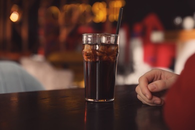 Man with glass of refreshing cola at table indoors, closeup. Space for text
