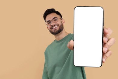 Happy man holding smartphone with empty screen on beige background, space for text