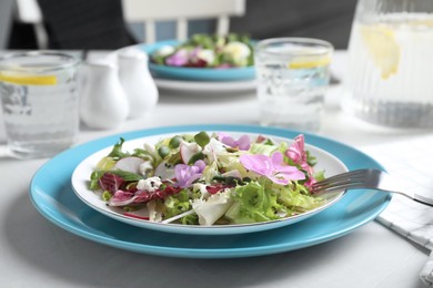 Photo of Fresh spring salad with flowers served on white table, closeup