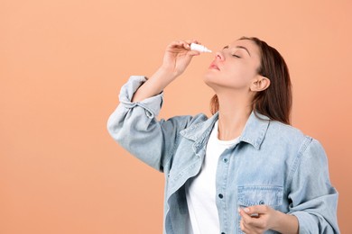 Woman using nasal spray on peach background, space for text